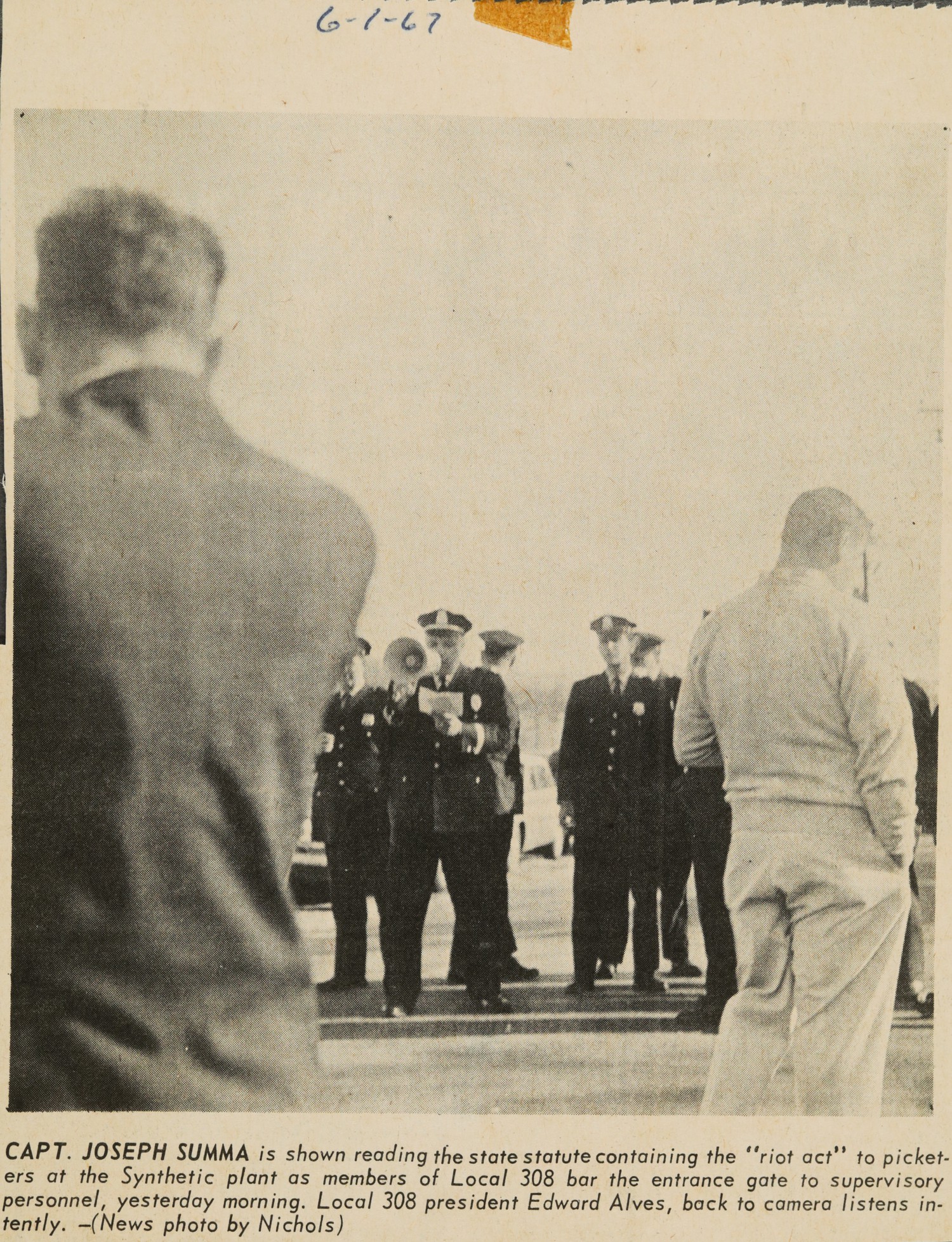 CAPT. JOSEPH SUMMA is shown reading the state statute containing the "riot act" to picketers at the Synthetic plant as members of Local 308 bar the entrance gate to supervisory personnel, yesterday morning. Local 308 president Edward Alves, back to camera listens intently.